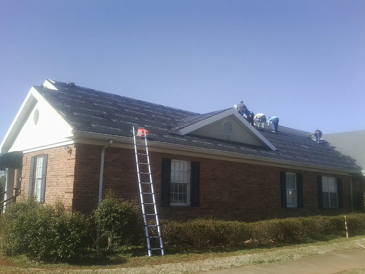 Crew tearing shingles off a brick ranch roof with a ladder set — Metal Roof Repair work by our crew in Atlanta