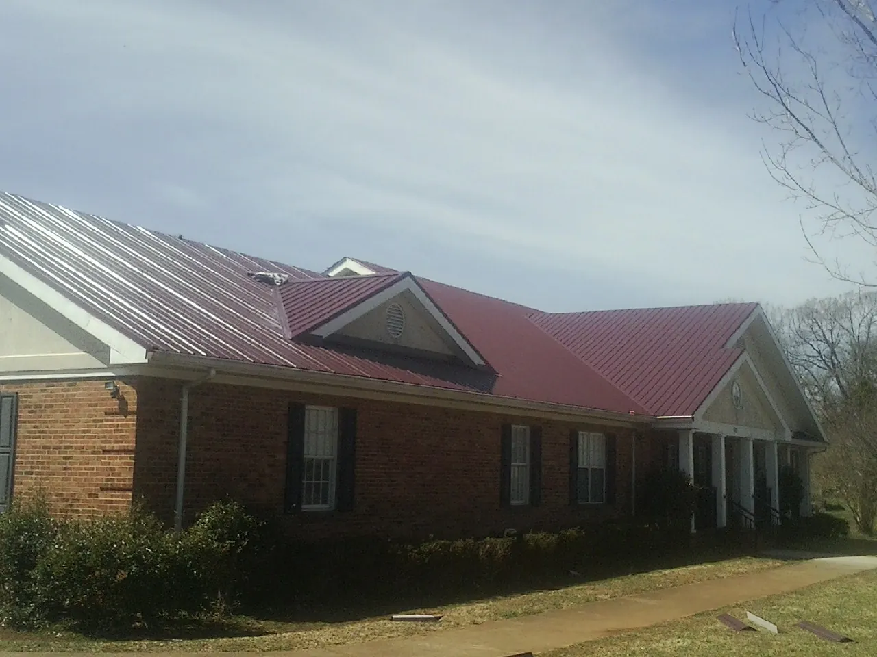 Red metal roof with gabled entries on a long brick building, from a Hail Damage Roof Repair job in Atlanta