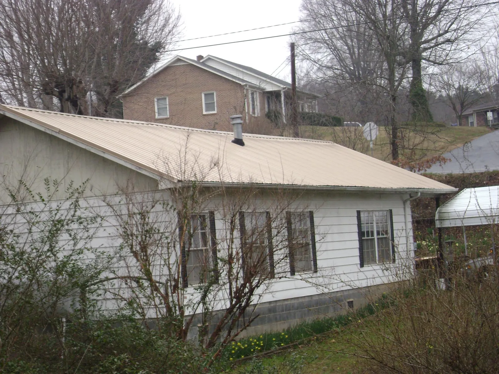 Tan metal roof on a white sided house set into a hillside — Commercial Roofing by Roofing Brothers in Atlanta